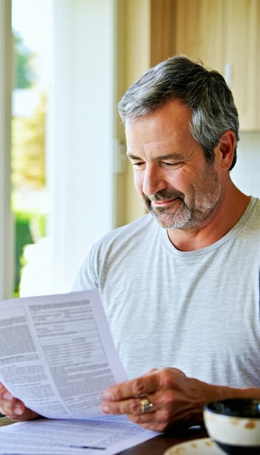 Calm and healthy adult patient sitting at home at a kitchen table reviewing a bill that came in the mail warm natural lighting soft blue and white tones